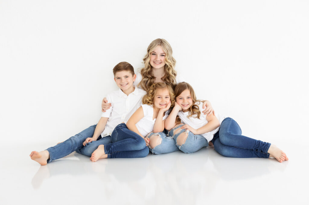 Four siblings sitting on the floor cuddled together.