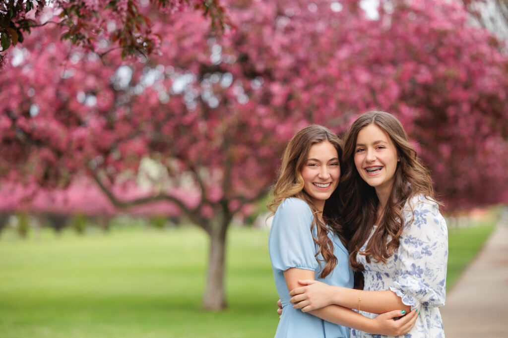 Sisters laughing and standing on tree lined path at Ann Morrison Park in Boise.
